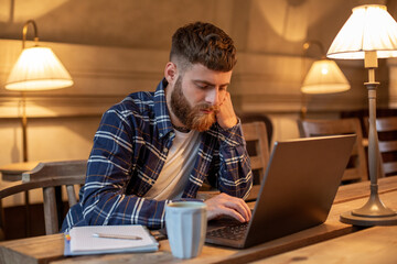 Young professional surfing the Internet on his laptop in a cafe