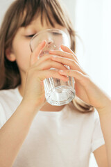 Close-up of a girl in the kitchen drinks clean water from a glass glass. Focus on the glass, face...