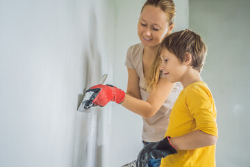 Woman with hir son makes repairs at home, she teaches boy to plaster the walls with a spatula in...