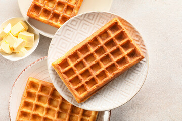 Plates with delicious Belgian waffles and butter on light background