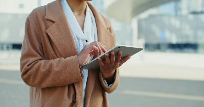 African American woman smiling while using a tablet while standing outdoors