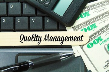 banknotes, pens, calculators and ice cream sticks with the words quality management