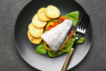 Plate of tasty sea bass fish with vegetables on black background