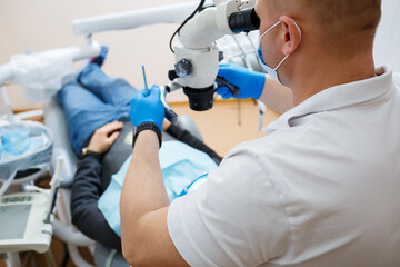 The dentist treats his patient's teeth with a microscope. The dentist treats the patient's mouth. Dental care