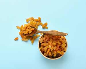 Bowl and spoon with tasty raisins on color background