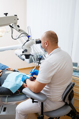 Naklejka na ściany i meble The dentist treats his patient's teeth with a microscope. The dentist treats the patient's mouth. Dental care