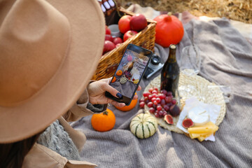 Young woman taking photo during romantic picnic on autumn day