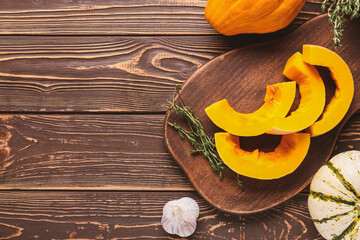 Board with fresh pumpkin pieces on wooden background