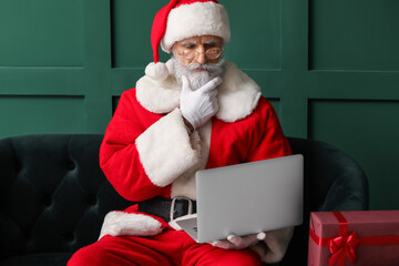 Thoughtful Santa Claus using laptop at home on Christmas eve