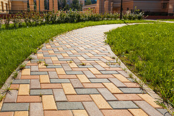 The pedestrian path is paved with multi-colored paving stones. Grass grows between the tiles....