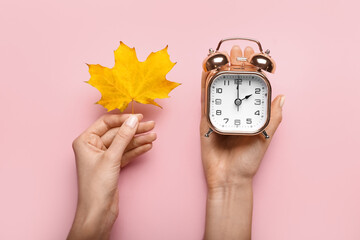 Female hands with alarm clock and autumn leaf on color background