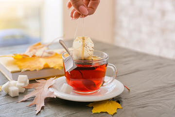 Female hand dipping tea bag in hot water at table in cafe