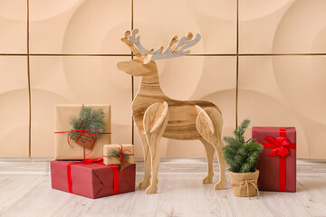 Wooden reindeer with small Christmas tree and presents near beige wall