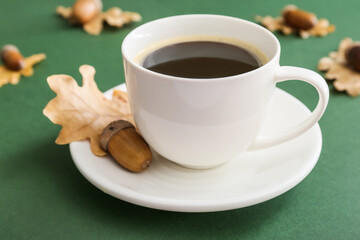 Cup of coffee with acorns on green background, closeup