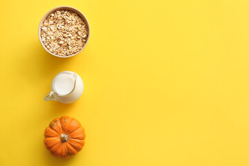Bowl with oatmeal flakes, pumpkin and jug of milk on yellow background