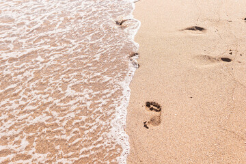 Human footprints on the sand with sea water. Foam from a wave on the sand with traces. A foamy ocean wave on a seashell beach