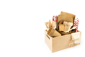 Wooden box with new fast food utensils. Disposable tableware set, wooden cutlery, pouches, glass bottle and paper cocktail tubes. Side view. Copy space
