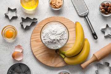 Bowl with flour, bananas and ingredients for preparing homemade cookies on light background
