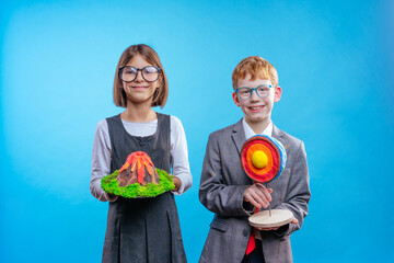 Two schoolchildren with eye glasses holding their scientific projects volcano and section of the...