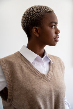 Trendy Black Woman With Short Hair And In White Shirt And Trendy Knitted Vest Looking Away On White Background