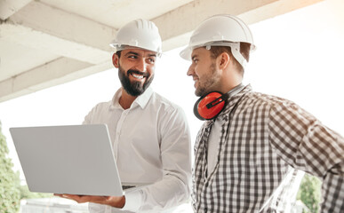 Smiling engineers discussing project while using laptop