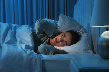 Unhappy young woman covering ears with pillow in bed at home. Noisy neighbours