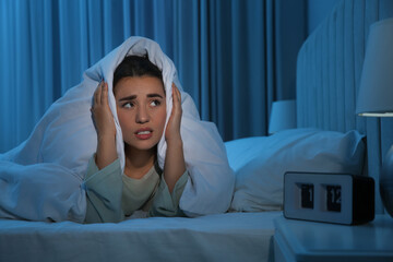 Unhappy young woman covering ears with blanket in bed at home. Noisy neighbours - obrazy, fototapety, plakaty