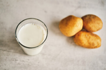A transparent glass with potato milk on the table next to the potato tubers. 