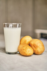 A transparent glass with potato milk on the table next to the potato tubers. 