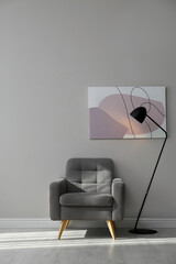 Stylish armchair and lamp near grey wall with beautiful picture. Interior design
