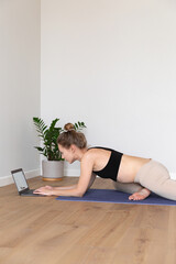 Obraz premium High quality photo of a young slim fit woman stretching at home, isolated in white room with wooden floor, using laptop, having online lesson, doing different sport exercise 