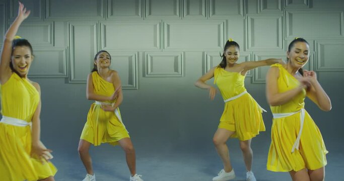 4k Group of beautiful , funny, stylish girls in yellow dresses dancing inside pavilion with grey background  . Synchronized dance of female ensemble for video clip  Woman dancers with the same outfit 