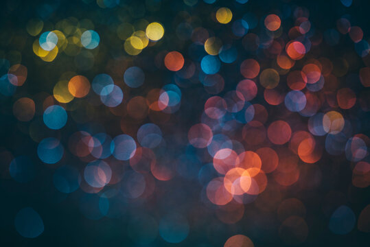 Neon bokeh background with blue, yellow and pink colors on black. Blur halftone art texture. Blurry night lights retro glow. Dark pastel circle abstract wallpaper photography.