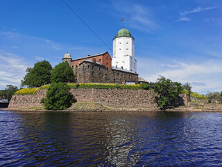 Fototapeta na wymiar View from the embankment of the Vyborg Castle and the St. Olaf Tower, built in the 13th century, in the city of Vyborg against the blue sky.