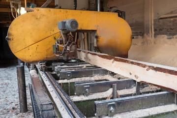 Fototapeta premium Processing wooden boards at a sawmill. The process of processing logs in the equipment of a sawmill saw a tree trunk on boards.