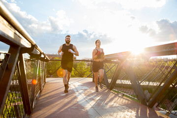 young Caucasian man and young Caucasian woman running on a bridge at sunset
