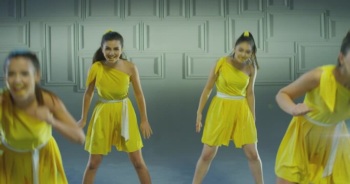 4k Group of beautiful , funny, stylish girls in yellow dresses dancing inside pavilion with grey background  . Synchronized dance of female ensemble for video clip  Woman dancers with the same outfit 