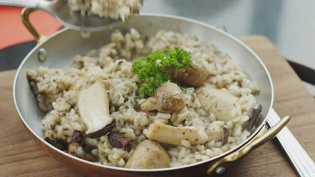 Close up 4K of risotto rice, which is traditional italian food menu, on the pan with spoon and fork using by people eating meal for lunch or dinner, and it looks delicious, yummy and healthy.