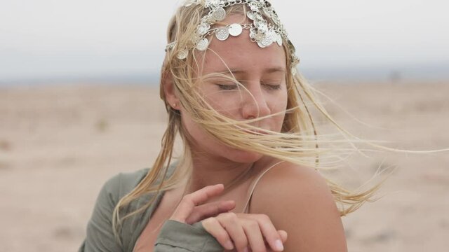 Hair of blondy woman with oriental jewelry swaing in the wind. Slow motion shot of dreamy, brooding and tender girl in the desert