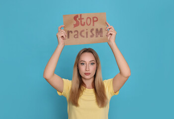 Young woman holding sign with phrase Stop Racism on light blue background