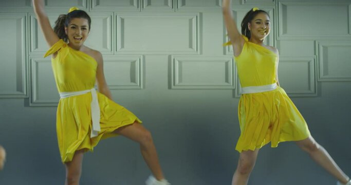 4k Group of beautiful , funny, stylish girls in yellow dresses dancing inside pavilion with grey background  . Synchronized dance of female ensemble for video clip  Woman dancers with the same outfit 