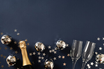 New Year champagne, wine glasses and shiny disco balls on blue navy background with copy space. View from above.