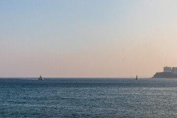 The sun is setting in the sky, the sea, a small boat, and a small lighthouse.