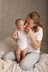 Mom hugs a cute blonde baby on a white bed. motherhood. breastfeeding. High-quality photography