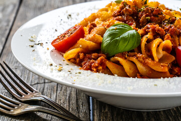 Fusilli with minced meat, tomato sauce, parmesan cheese and basil served on wooden table
