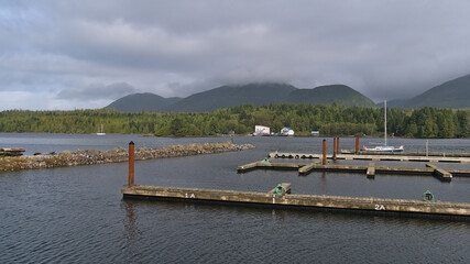 View of mostly empty jetty in the harbour of village Ucluelet on Vancouver Island, British Columbia, Canada on cloudy day in autumn with sailing boat.