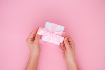 Female hands are holding a gift box on a pink background, copy space. Gifts and presents concepts. View from above.