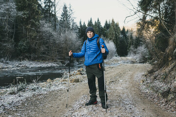 Man with trekking poles hiking in Winter forest
