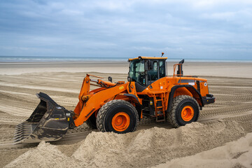 orange bulldozer on the beach is digging in the sand at Berck sur mer / France / Côte d'Opale
