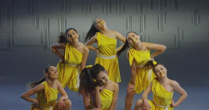4k Group of beautiful , funny, stylish girls in yellow dresses dancing inside pavilion with grey background  . Synchronized dance of female ensemble for video clip  Woman dancers with the same outfit 